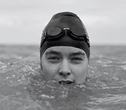 A swimmers head above water in a cap and goggles