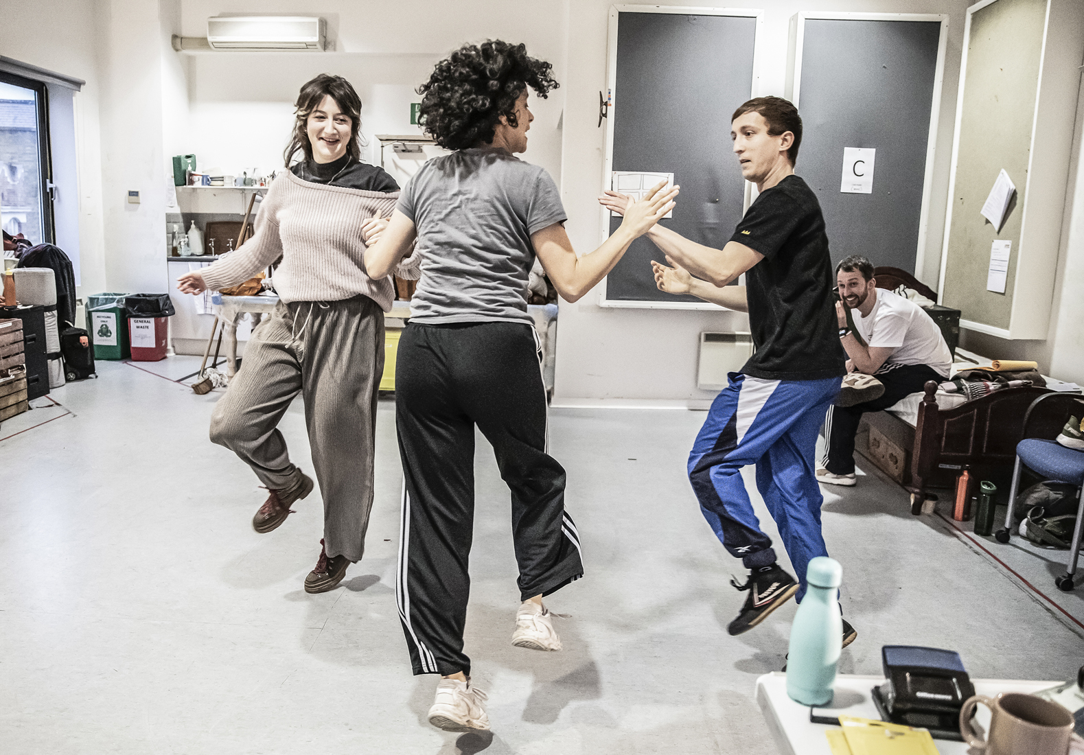 In the rehearsal room, Rebecca Banatvala, AK Golding, and Sam Newton join hands and dance in a circle together.