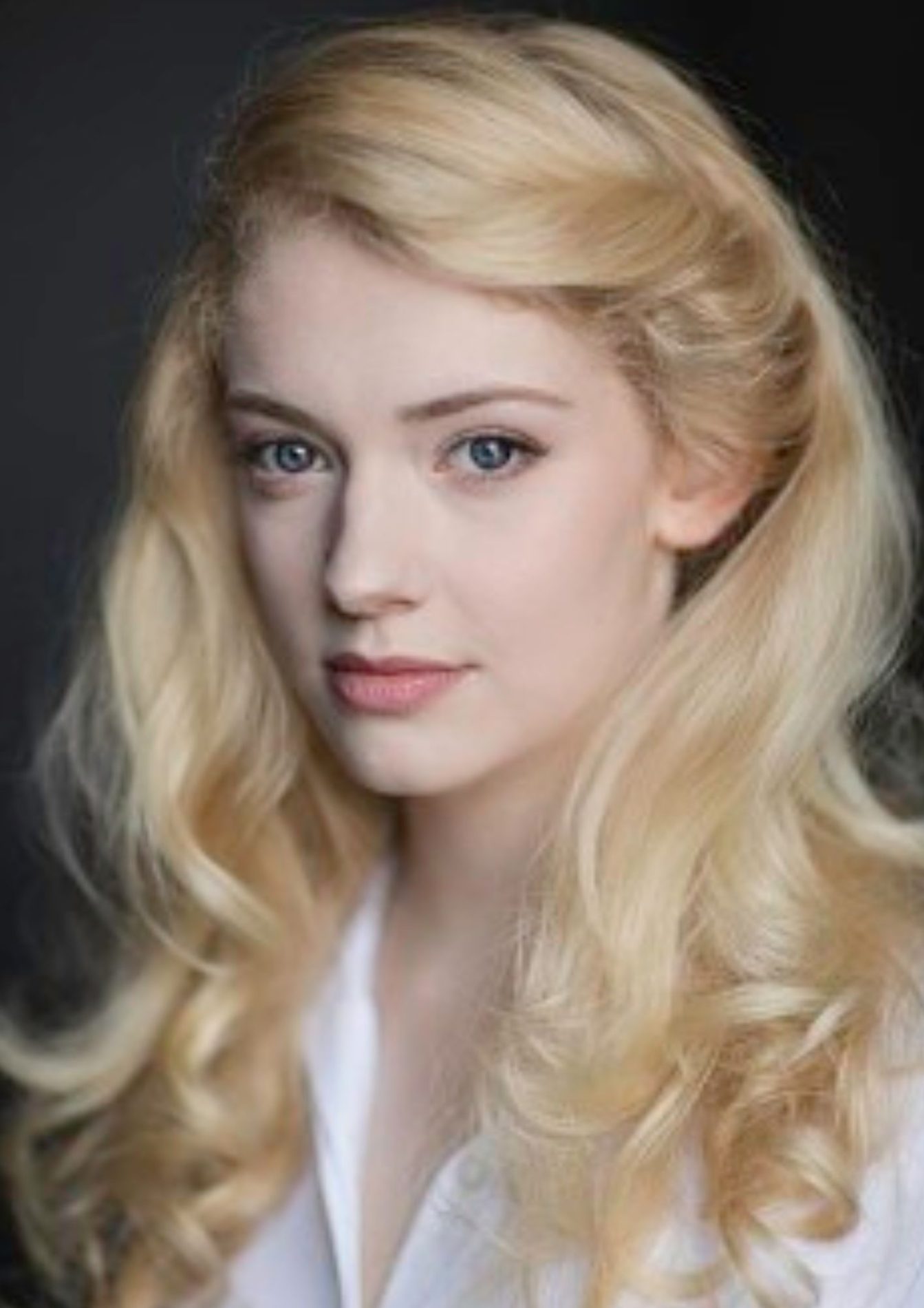 Lily Sacofsky's headshot: She wears a white button up shirt and has blond hair that is styled in curls.