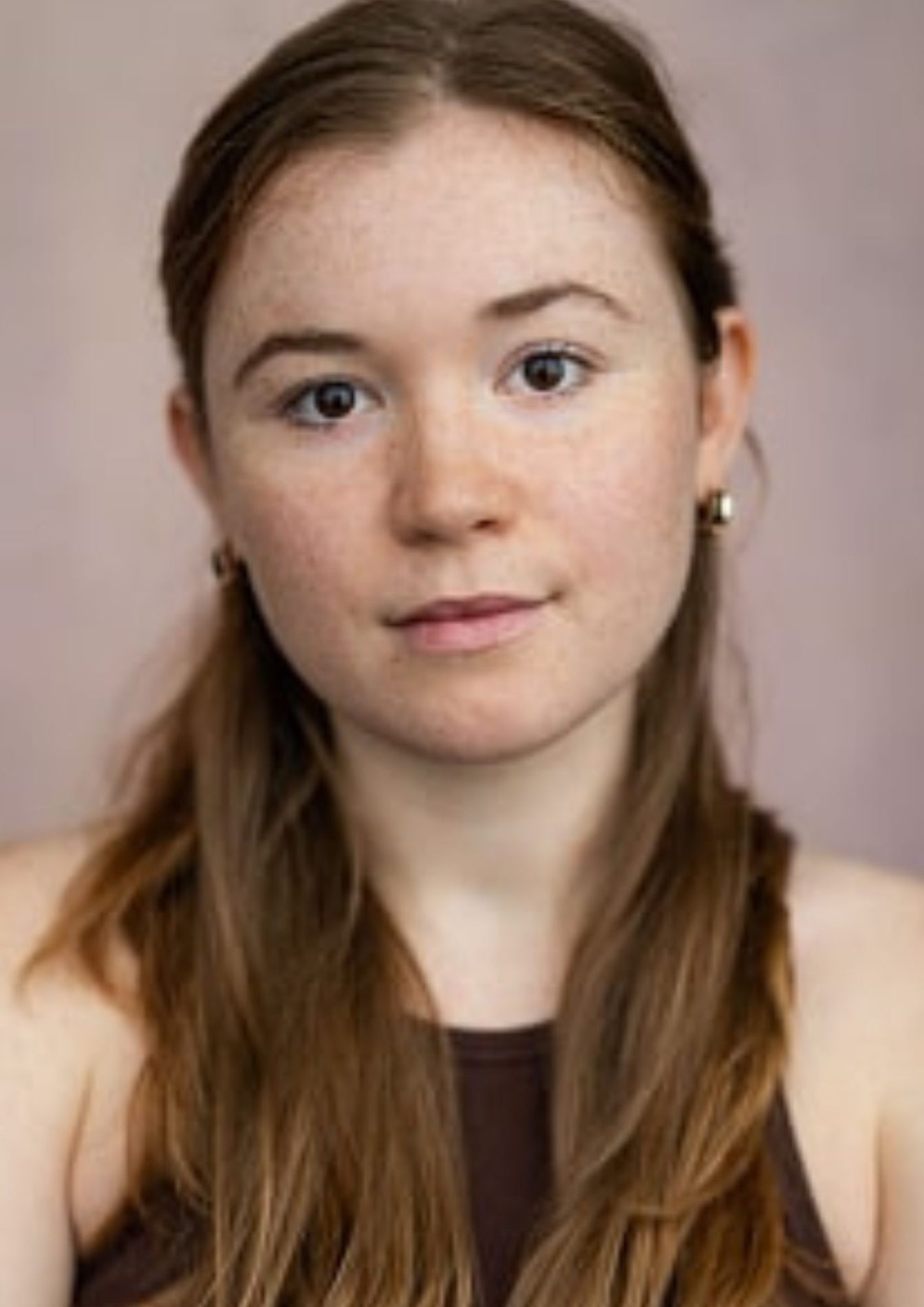 Madeleine Gray's headshot: She has reddish-brown hair that is partially pulled back. She has brown eyes, freckles, and wears a black tank top.